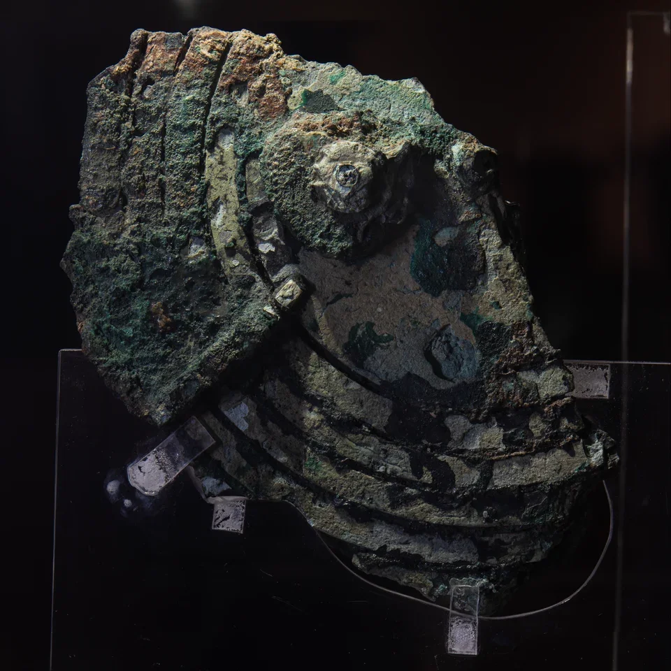 Fragment B du mécanisme d’Anticythère, en bronze corrodé, avec un axe et des éléments de cadran visibles.